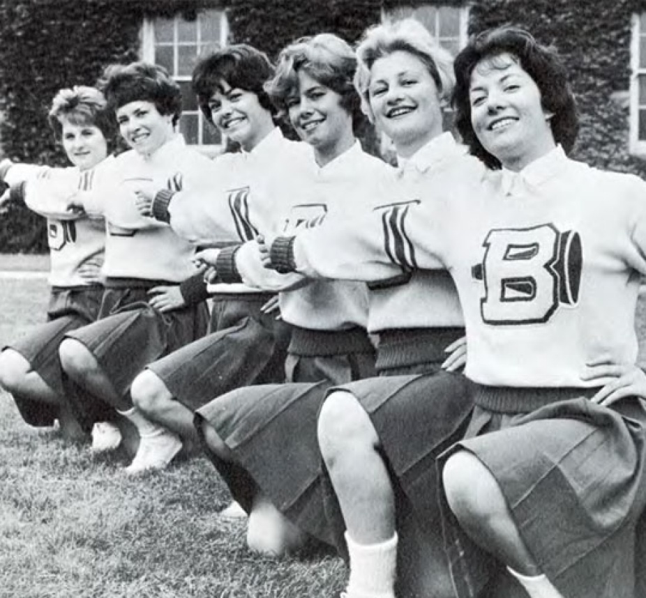 In black and white, a row of smiling cheerleaders. 