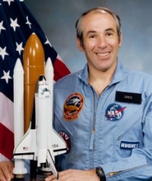 Gregory B. Jarvis headshot in front of the American flag and next to a model rocket. 