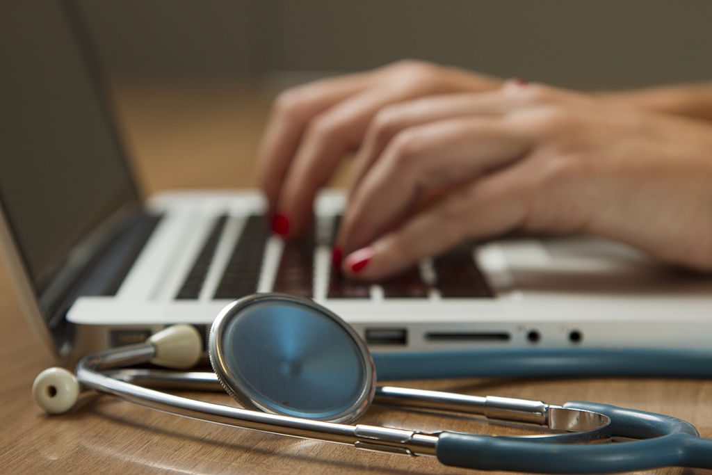 Photo of hands typing on laptop with a stethoscope sitting on a desktop